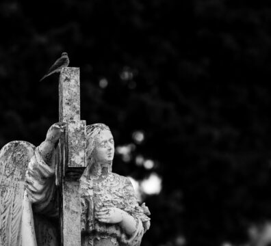 An angel statue holding a cross topped with a small bird, symbolizing peace and spirituality, against a dark, serene background.