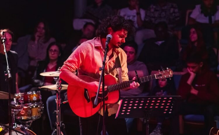 A photo showing a guitarist in live concert with the audeince behind him