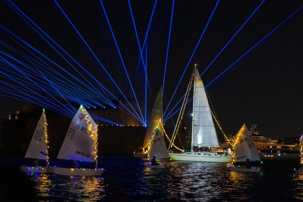 A photo showing Illuminated water fountains and sailing vessels during the Valletta Pageant of the Seas in Malta's Grand Harbour.